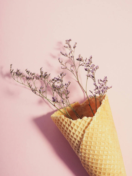 Μπουκέτο με αποξηραμένα λουλούδια σε φλυτζάνι βάφλας από παγωτό, χωνάκι, σε ροζ φόντο, μινιμαλισμός. - Φωτογραφία, εικόνα