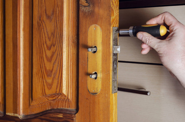 Muž odemyká starý zámek dveří. Ruce se šroubovákem odšroubují montážní šrouby zdvíhacího zámku dřevěných vnitřních dveří. Služby opravy nebo výměny nábytku. Indoors - Fotografie, Obrázek