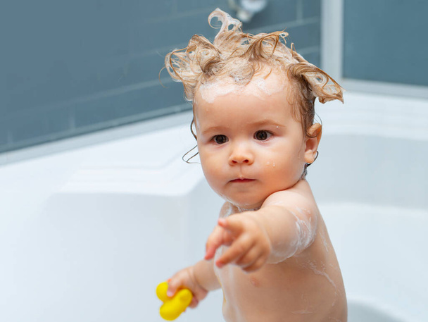 Funny blond kid boy having fun with water by taking bath in bathtub. Bathing baby. Happy kid with soap foam on head. - Foto, Bild