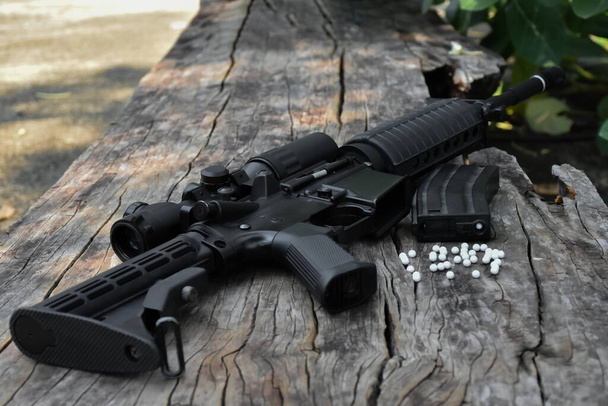 Pistola bb o airsoft automática de cañón largo negra en pisos de madera con balas de plástico blanco. Enfoque suave y selectivo. - Foto, imagen