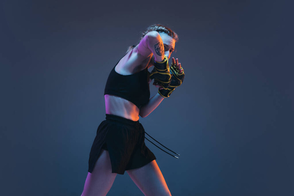 Caucasian female MMA fighter training isolated on blue background in neon light - Photo, Image