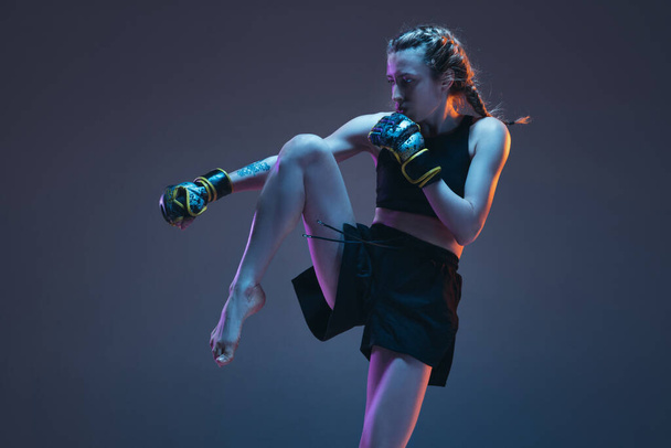 Молода жінка - боєць MMA, ізольований над синім фоном у неоновому світлі. - Фото, зображення
