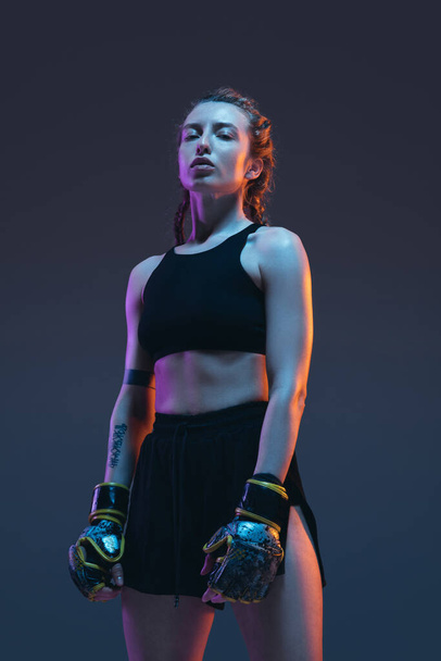 combattant MMA femme caucasienne posant isolé sur fond bleu dans la lumière au néon - Photo, image