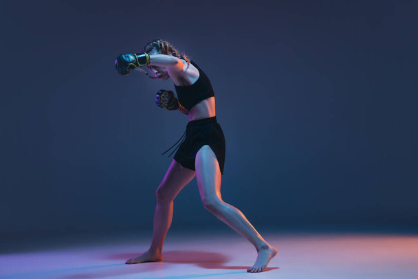 Caucasian female MMA fighter training isolated on blue background in neon light - Foto, afbeelding