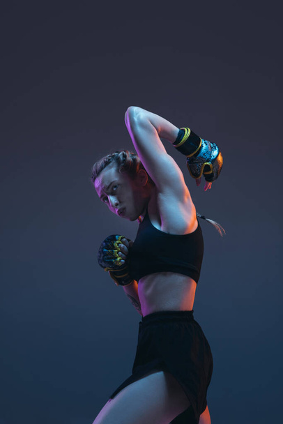 Blanke vrouwelijke MMA gevechtstraining geïsoleerd op blauwe achtergrond in neon licht - Foto, afbeelding