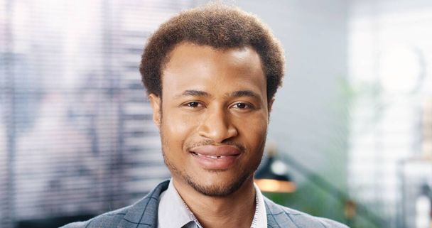 Close up of handsome African American happy young man looking at camera and smiling indoors in good mood. Cheerful male worker with smile on face. Businessman with positive emotions - Photo, image