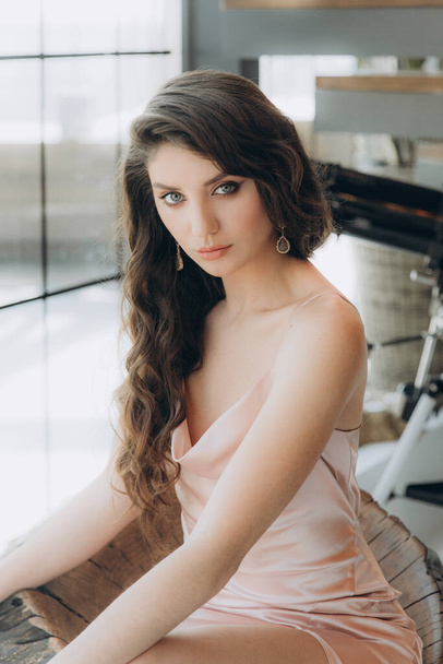 Beautiful, stylish, and elegant girl brunette, model, with makeup and curly hair in a peach-colored silk dress for a magazine photoshoot in fashion style. - Fotografie, Obrázek