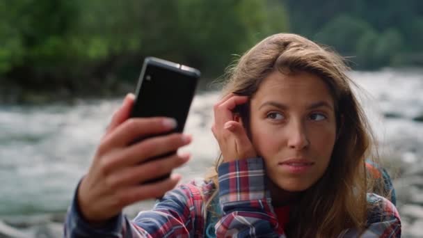 Турист фиксирует волосы перед видеочатом на смартфоне. Девушка машет рукой в камеру - Кадры, видео