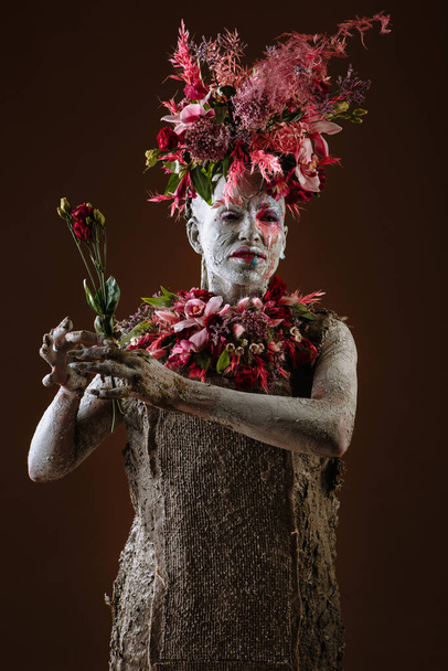 A girl smeared with clay. The model has a headdress made of flowers. - Foto, Imagem