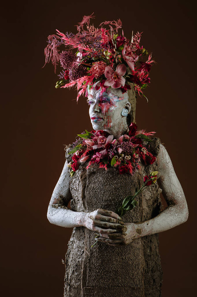 A girl smeared with clay. The model has a headdress made of flowers. - Φωτογραφία, εικόνα