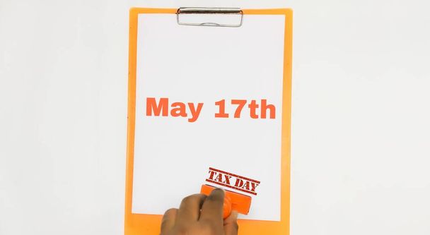 Closeup of A4 Sheet nyírt egy vágólapon május 17-én és kézi bélyegzés Adónap egy elszigetelt fehér háttérrel. Pénzügy. Adózás. - Fotó, kép
