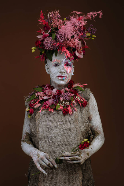 A girl smeared with clay. The model has a headdress made of flowers. - Foto, imagen