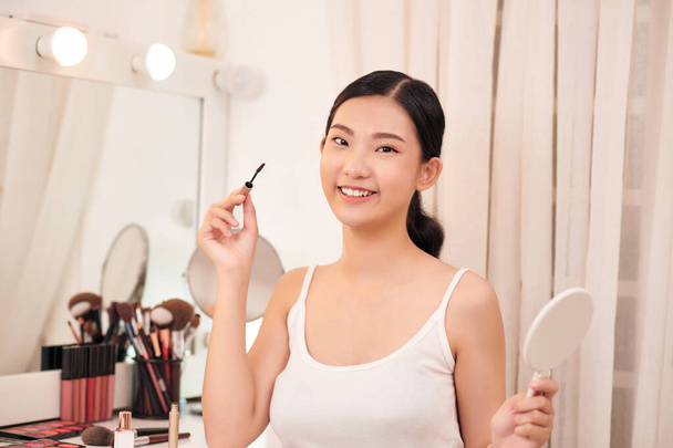 Красивая молодая женщина наносит макияж возле зеркала в гримерной - Фото, изображение