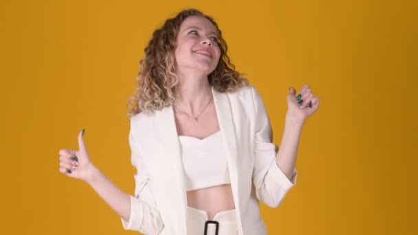 Positive young attractive girl with curly hair posing isolated on yellow studio background. Woman Looking approvingly at camera showing thumbs up, like sign positive something good. People lifestyle - Filmmaterial, Video