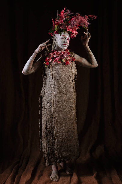 A girl smeared with clay. The model has a headdress made of flowers. - Valokuva, kuva