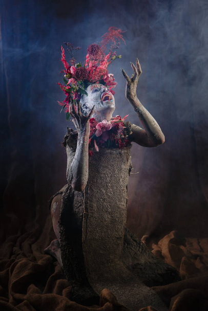 A girl smeared with clay. The model has a headdress made of flowers. - Photo, image