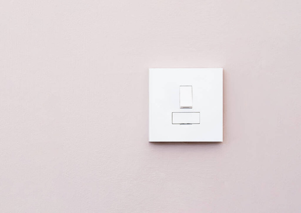 Interruptor de luz isolado na parede roxa clara, um interruptor mecânico de plástico de cor branca instalado na parede para ligar ou desligar as luzes dentro da sala. - Foto, Imagem
