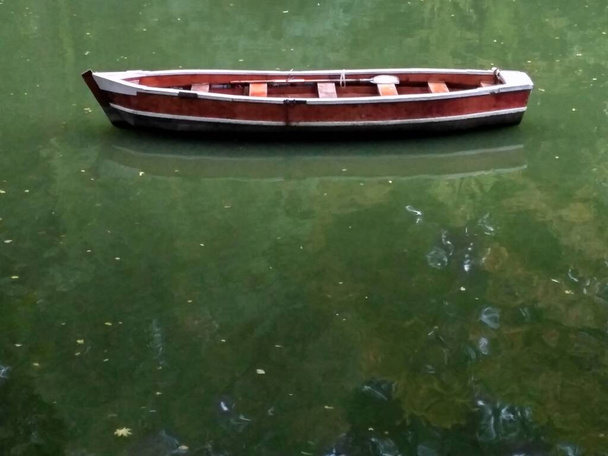 Wooden boat without people with green lake water reflection, row boat side view. - Photo, Image