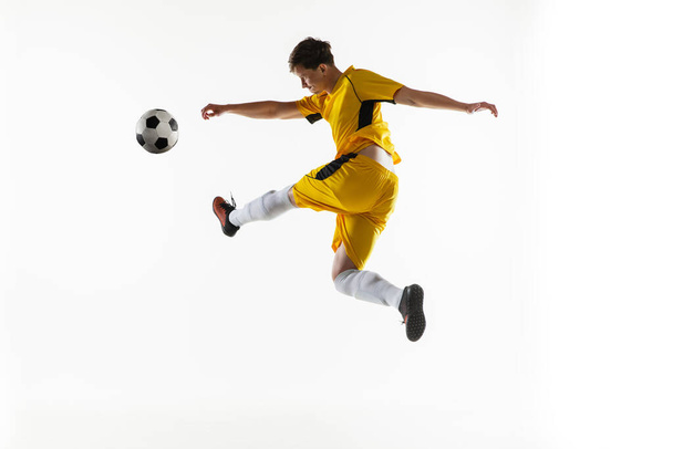 Νεαρός, αρσενικό ποδοσφαιριστής προπόνηση απομονώνονται σε λευκό φόντο. - Φωτογραφία, εικόνα