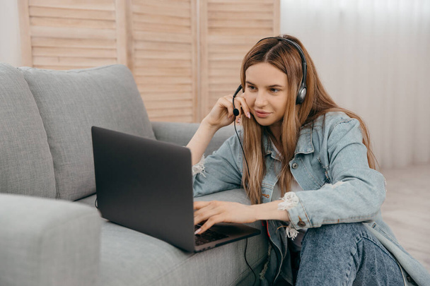 Улыбающаяся девушка-подросток носит наушники и смотрит на экран компьютера смотреть вебинар или делать видео-чат с веб-камеры - Фото, изображение