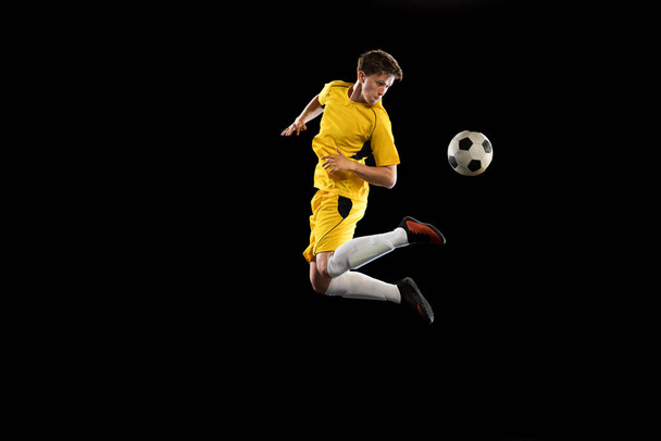 Young man, male soccer football player training isolated on black background. - Фото, изображение