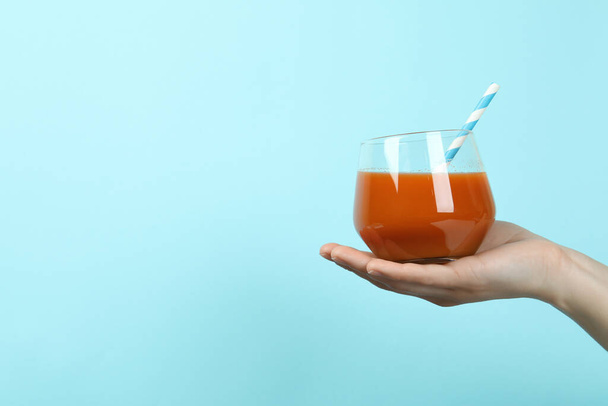 Female hand hold glass of juice on blue background - Фото, изображение