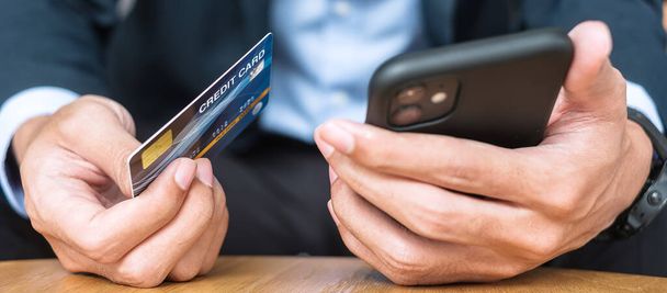 スーツを着たビジネスマンは、クレジットカードを保持し、カフェやオフィスで注文しながら、オンラインショッピングのためのタッチスマートフォンを使用しています。 - 写真・画像