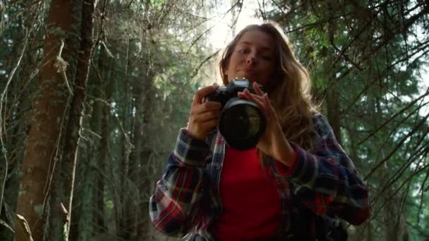 Nainen katselee kameraa. Naisvalokuvaaja ottaa kuvia metsämaisemasta - Materiaali, video