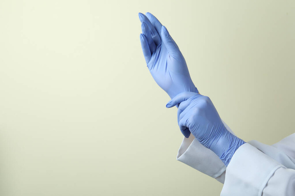 Doctor zetten medische handschoenen op licht beige achtergrond - Foto, afbeelding