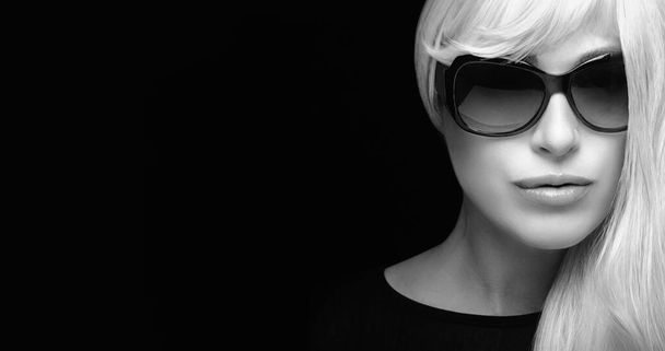 Retrato de moda de uma mulher loira atraente com cabelos brancos prateados longos, usando óculos escuros pretos, olhando para a câmera. Retrato de close-up monocromático isolado em fundo preto com espaço de cópia para texto - Foto, Imagem
