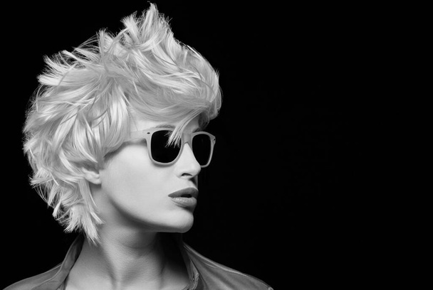 Beauty fashion model girl with modern blond short hairstyle  wearing sunglasses. Monochrome profile closeup portrait, isolated on black - Photo, image