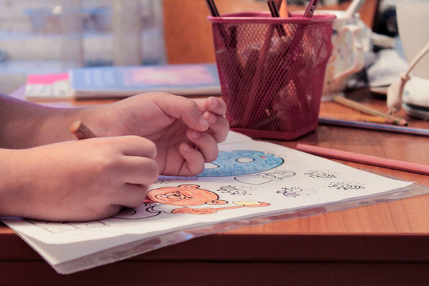 Közelkép Toddler kezét, ahogy festi a kifestőkönyv. A kisgyermekkori fejlődés és kreativitás fogalma. - Fotó, kép