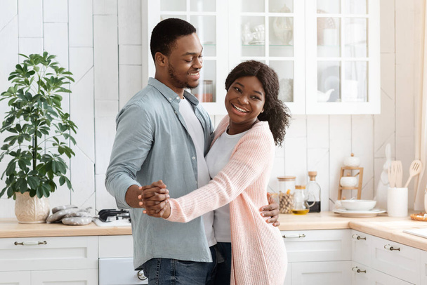 Felices cónyuges negros alegres teniendo momentos románticos en casa, bailando en la cocina - Foto, Imagen