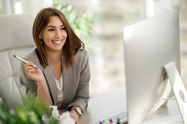 Usmívající se podnikatelka sedící sama ve své kanceláři a pracující na počítači. - Fotografie, Obrázek