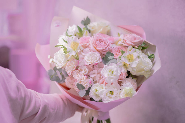 A man's hand holds a lush bouquet of light pink, white cute delicate small roses of different sizes, flowers of green leaves. Paper packaging. Romance. - Foto, Imagem