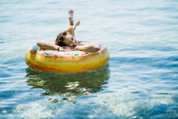 Güzel genç bir kadın deniz suyunda şişme yüzükle yüzüyor ve tatilin tadını çıkarıyor.. - Fotoğraf, Görsel