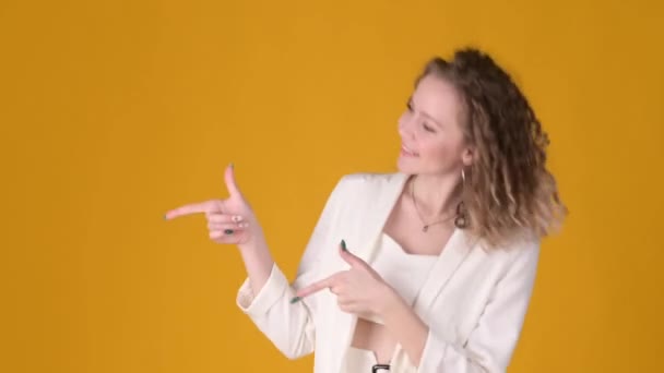 Young Cheerful expressive girl with curly hair and pointing fingers hands aside on copy space workspace area isolated on yellow background. People lifestyle concept. - Video