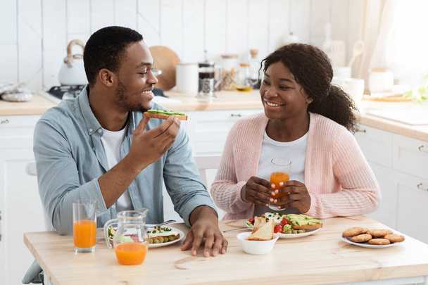 Alegre afroamericano cónyuges comiendo comida en cocina y tener charla - Foto, Imagen