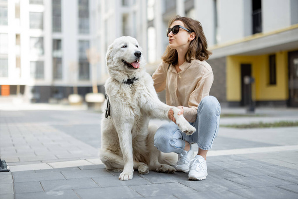 Frau läuft mit ihrem großen weißen Hund auf der Straße - Foto, Bild