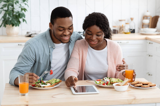 Junge schwarze Millennial-Ehepartner kaufen beim Frühstück online auf einem digitalen Tablet ein - Foto, Bild