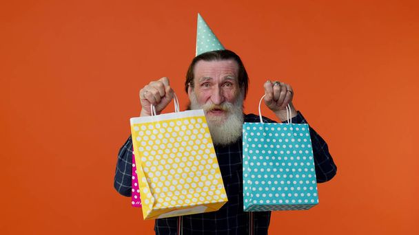 Літній бородатий чоловік показує сумки для покупок, рекламні знижки, дивується низькими цінами
 - Фото, зображення