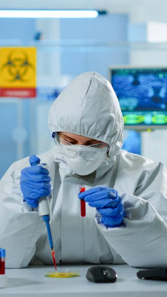 Tiedeteknikko ppe-puvussa käyttäen mikropipettiä ja petrimaljaa verinäytteen analysoinnissa - Valokuva, kuva