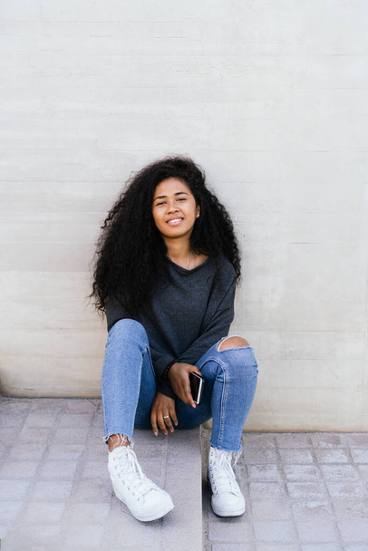 Portrait of a happy afro teenager smiling with a mobile phone - Photo, image