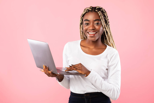 Smiling young black lady holding and using laptop at studio - Foto, Bild