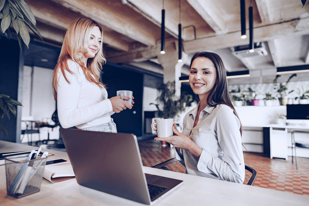 Two young women colleagues drinking coffee in office - Foto, imagen