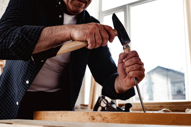 Die Hände eines Tischlers, der mit Meißel und Hammer arbeitet - Foto, Bild