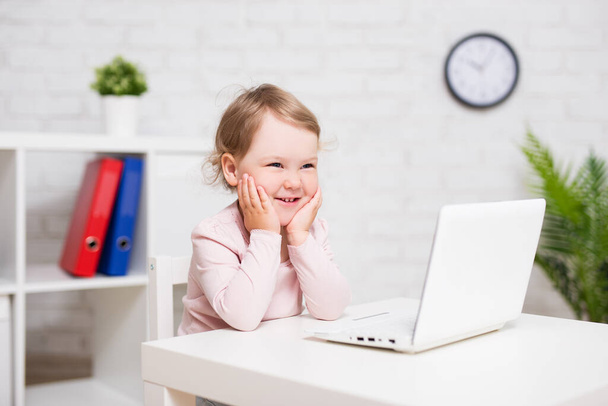 childhood, education, business and technology concept - cheerful little girl using laptop at home or in class room - Photo, Image