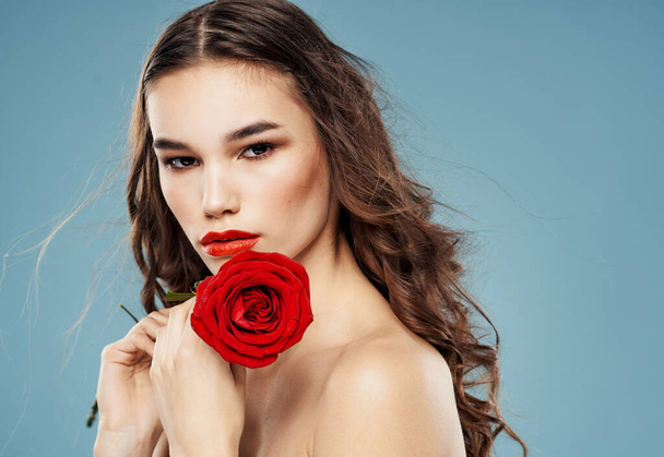Young woman with red rose near face shadow on eyelids blue background model - Foto, imagen