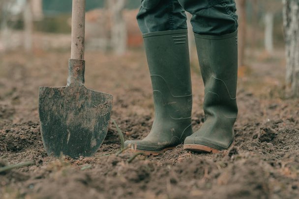 Farmer in rubber boots using spade gardening equipment in garden, low angle, selective focus - Foto, afbeelding