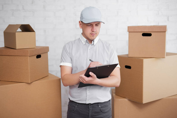 podnikatelům a konceptu poštovních zásilek - doručovatel v uniformě něco kontroluje na schránce mezi krabicemi - Fotografie, Obrázek